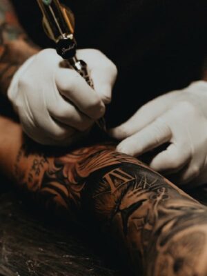 Tatuador profissional aplicando tatuagem no braço de um cliente no estúdio Art Brilho Ink Tatuapé.