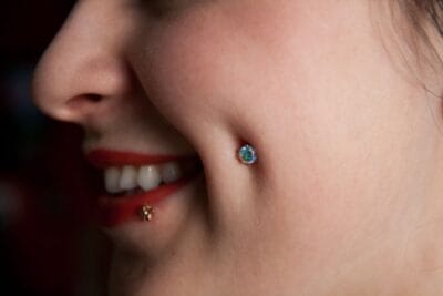 Piercing na bochecha recém-aplicado com joia de aço cirúrgico em estúdio profissional no Tatuapé.