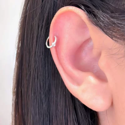Piercing hélix já aplicado na orelha com joia delicada e acabamento profissional no estúdio Art Brilho Ink no Tatuapé.
